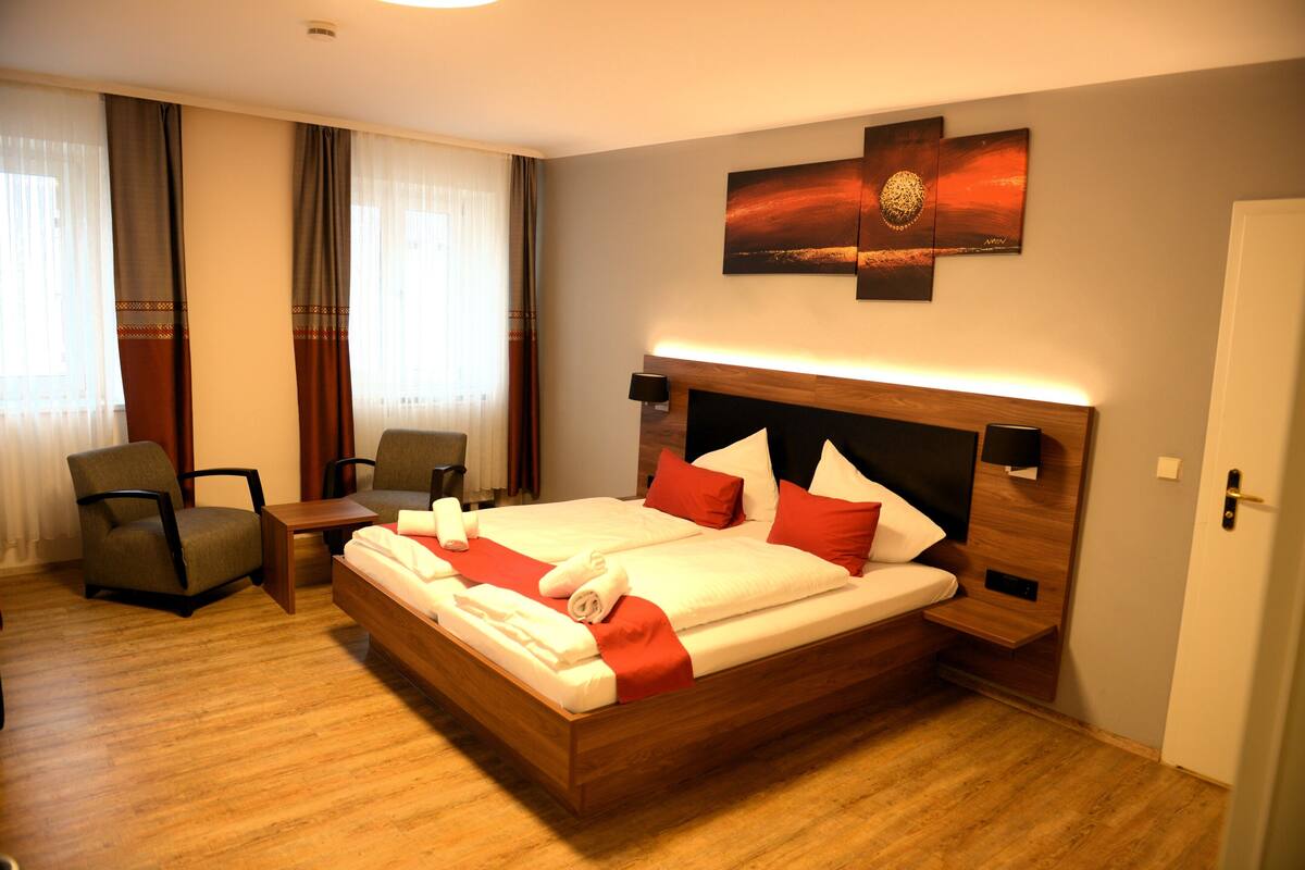 Una habitación de hotel con una cama grande, dos mesitas de noche, una silla y un escritorio.