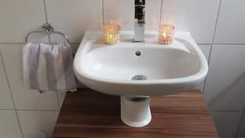Ein Badezimmer mit einem weißen Waschbecken, zwei brennenden Kerzen und einem Handtuch an einem Haken.