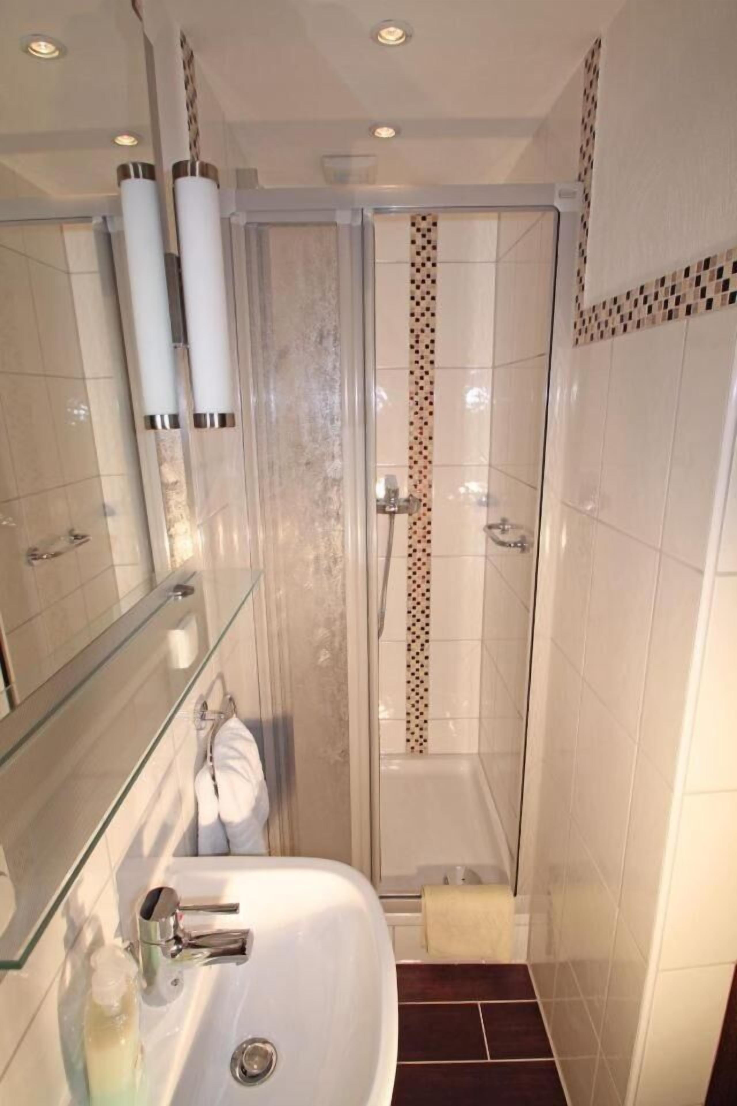 Een moderne badkamer met een douchecabine van glas, een witte wastafel en een glazen opbergmeubel.