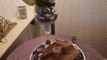 Un cuenco decorativo con un trozo de chocolate encima, rodeado de piedras pequeñas y una flor blanca en un florero de vidrio.