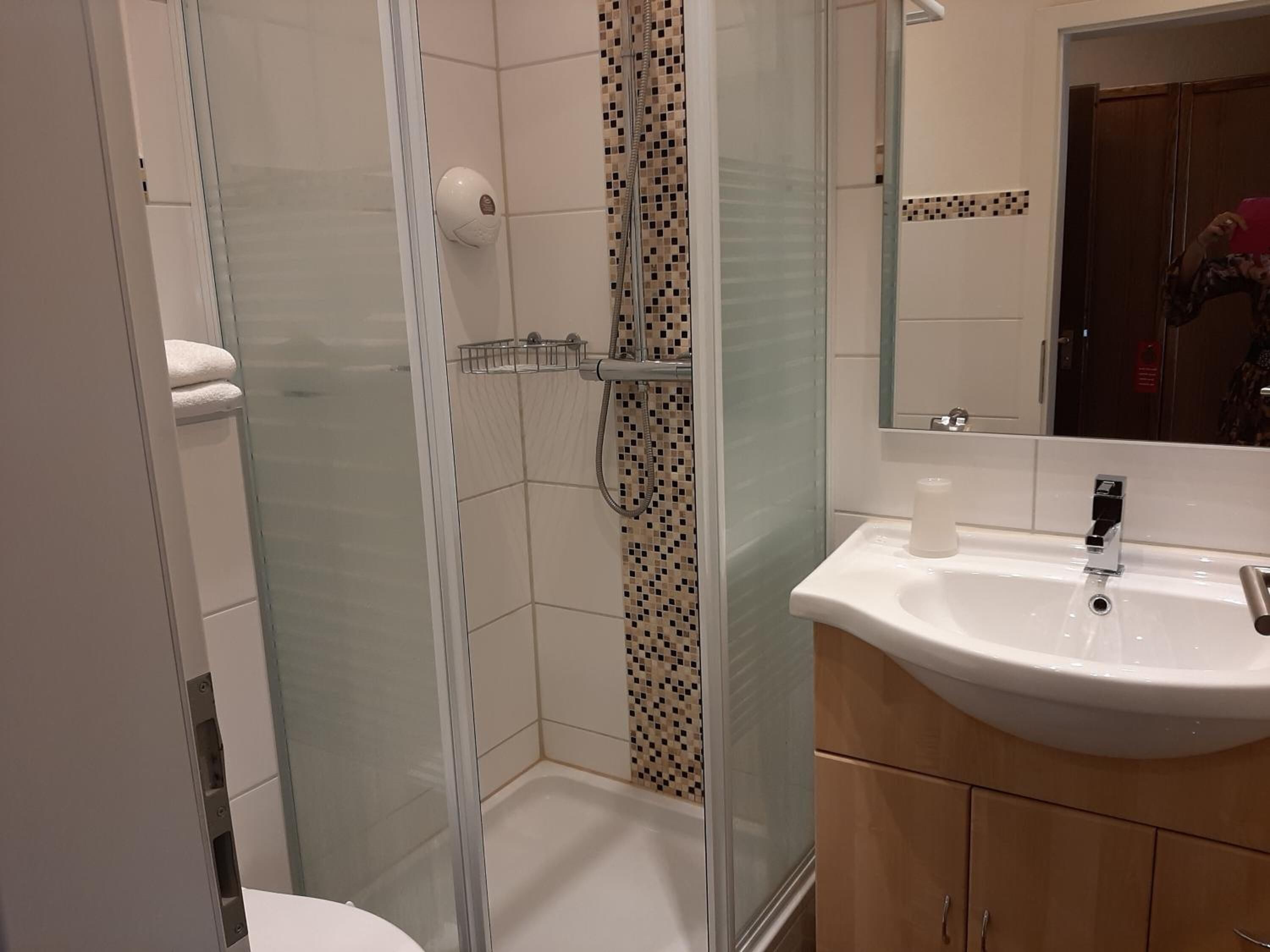 Ein Badezimmer mit Duschkabine aus Glas, einem weißen Waschbecken und einem Spiegel darüber.