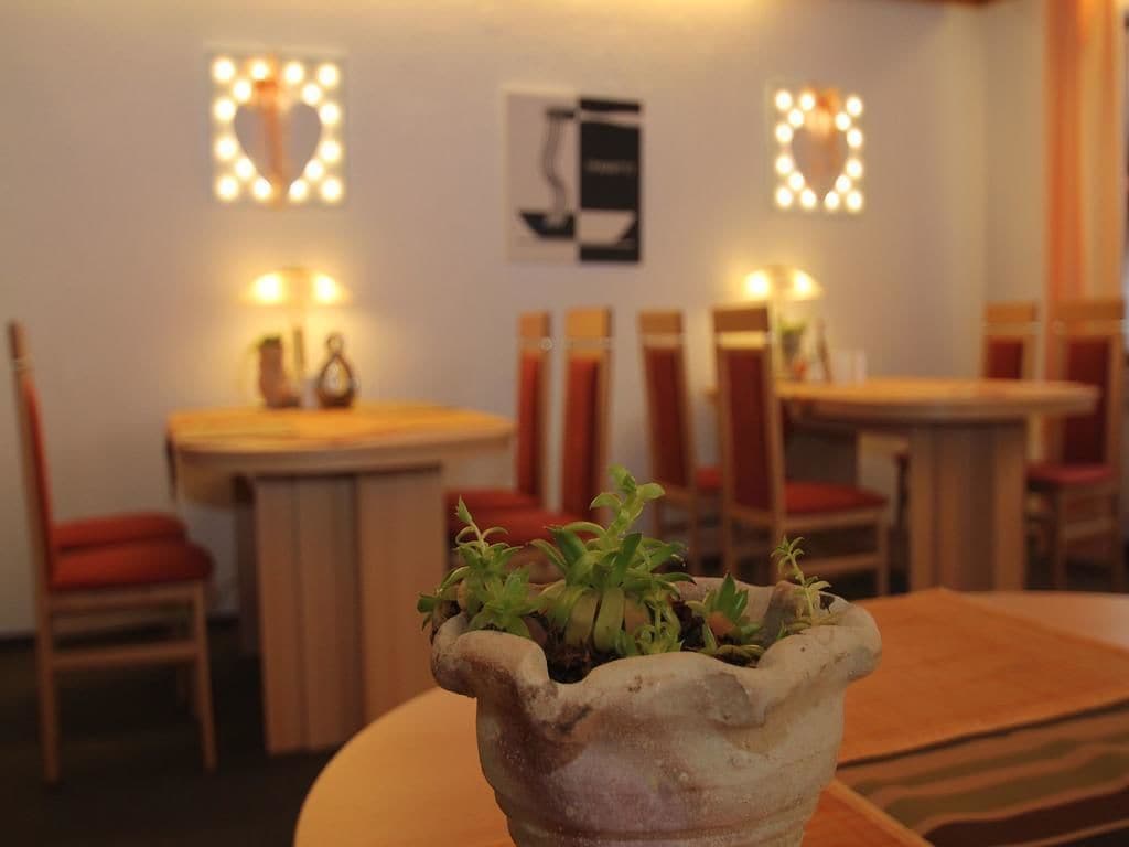 A dining area with tables and chairs, a potted plant in the foreground, and wall-mounted light fixtures.