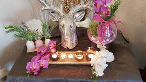 A table with a decorative centerpiece featuring a silver deer head, surrounded by small potted plants and pink orchids. - Hotel Irene (Bad Konig)