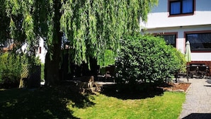 A white building with a patio area, a large tree, and a well-maintained lawn. - Hotel Irene (Bad Konig)