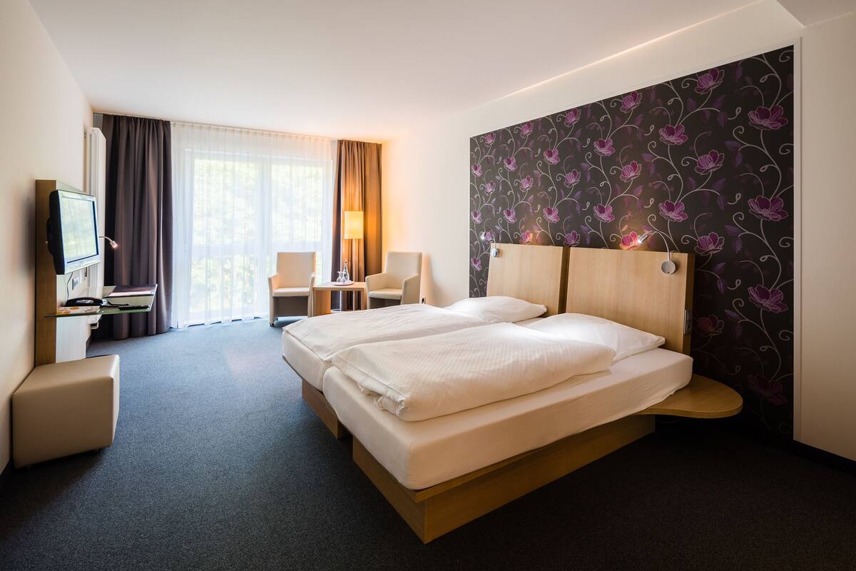 A hotel room with a large bed, a desk with a chair, a TV, and a window with curtains.