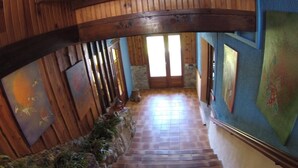 Una escalera de madera con un muro de piedra a un lado y un muro azul al otro, que conduce a una puerta.