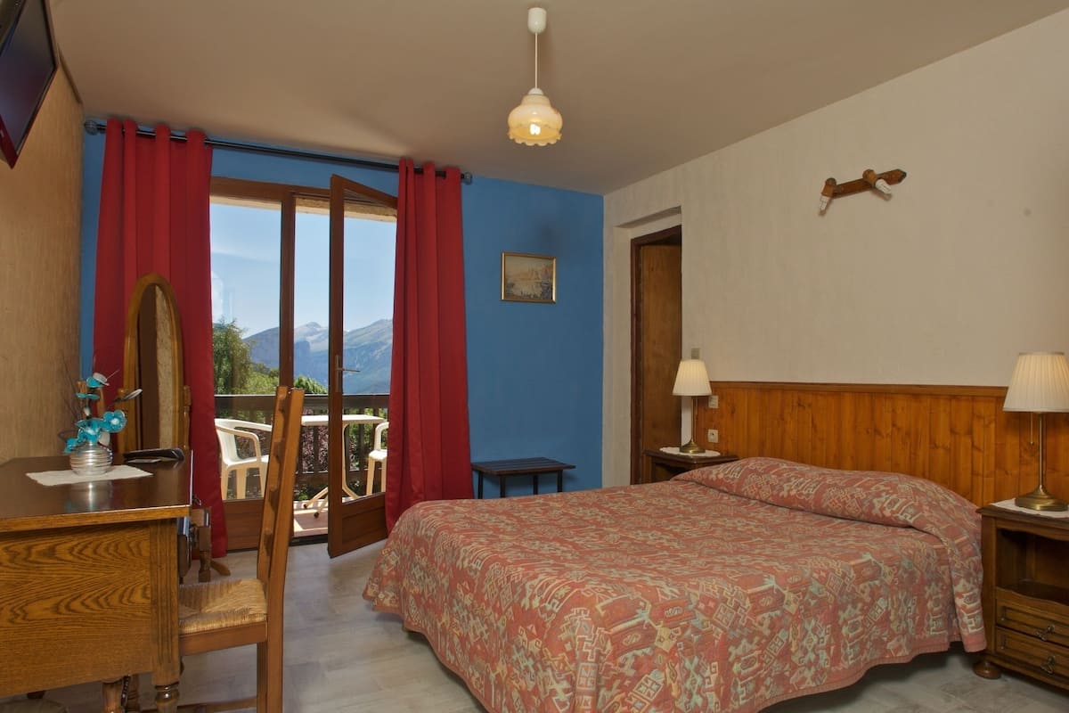 Ein Schlafzimmer mit einem Bett, einem Schreibtisch, einem Sessel, einem Nachttisch und einem Fenster mit Vorhängen.