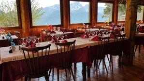 Un restaurante con varias mesas dispuestas para comer, amplias ventanas con vistas a la montaña y diseño de interiores de madera.