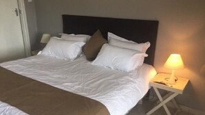 Un lit bien fait, avec une literie blanche et marron, une lampe de chevet et un mur sobre.