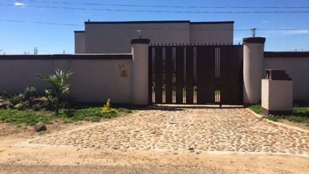 Un bâtiment doté d’une entrée fermée par un portail, d’une allée pavée et d’un mur blanc agrémenté d’un petit jardin.