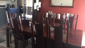 Un coin repas avec une table et des chaises en bois, un mur rouge et une cuisine en arrière-plan.