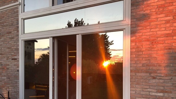 A modern building with large glass doors and windows, reflecting a sunset. - B&B Il Melograno (Formigine)