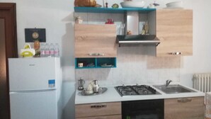 Een kleine keuken met een koelkast, fornuis, spoelbak en houten kastjes.