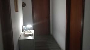 Een smalle gang met een houten deur aan het einde, een kleine tafel met een lamp en een lijst met een afbeelding aan de muur.
