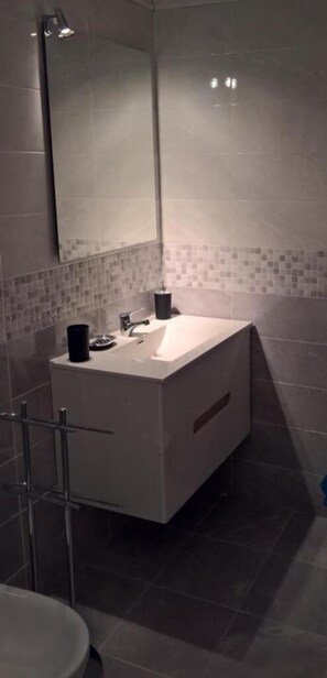 Une salle de bain moderne avec un meuble-lavabo blanc, un grand miroir et un pare-feu en carreaux.