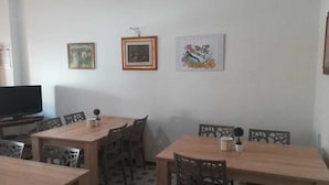 Een eetgedeelte met een houten tafel en stoelen, een televisie op een standaard en drie ingekaderde foto's aan de muur.