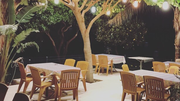 An outdoor dining area with tables and chairs under a tree with hanging lights. - Camyuva Motel (Kemer)