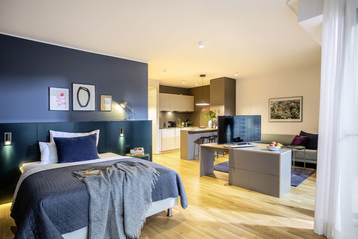 Ein modernes Hotelzimmer mit Bett, Schreibtisch, Fernseher und einer Küchenzeile.