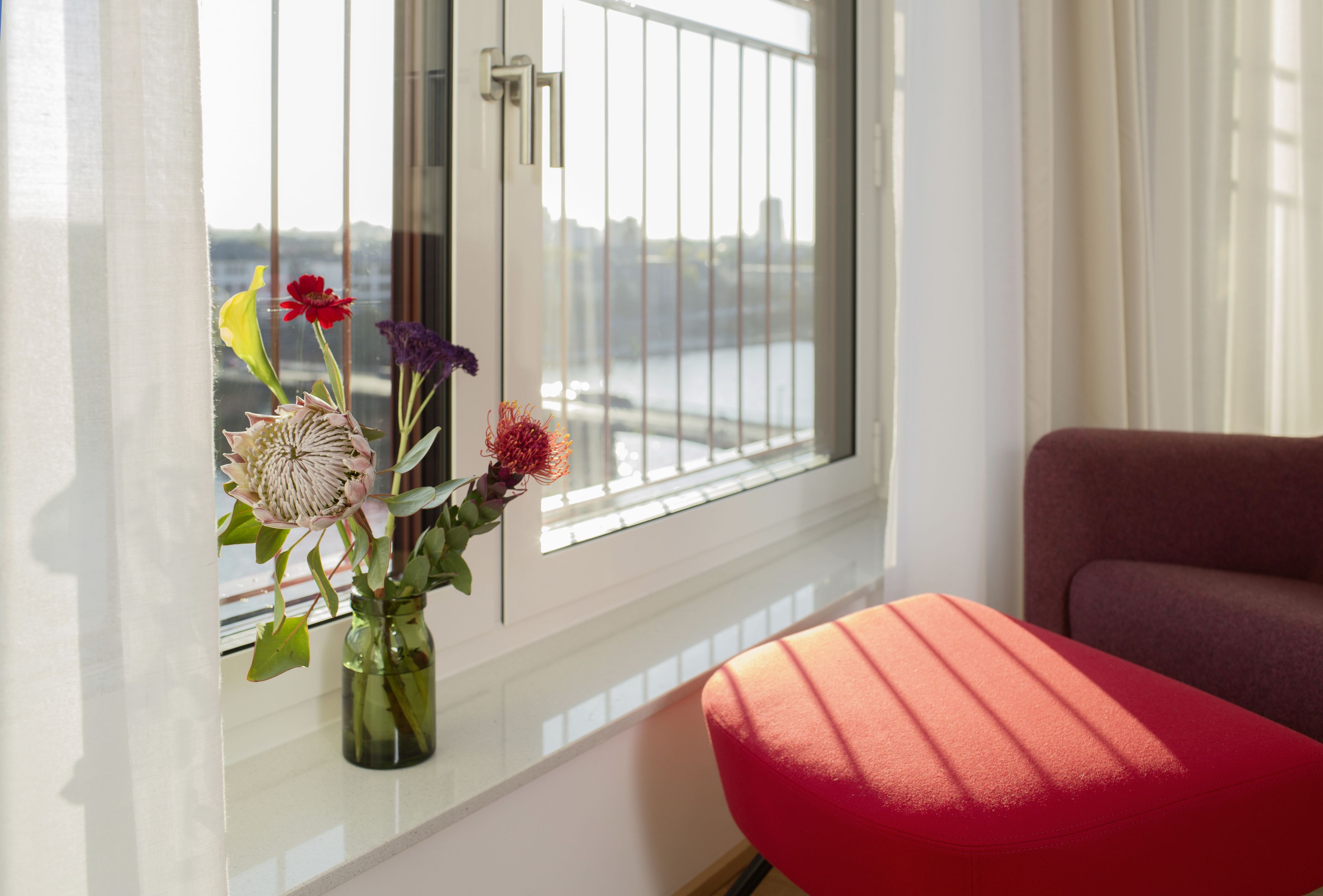 Una habitación con ventana, un jarrón con flores y una silla roja.