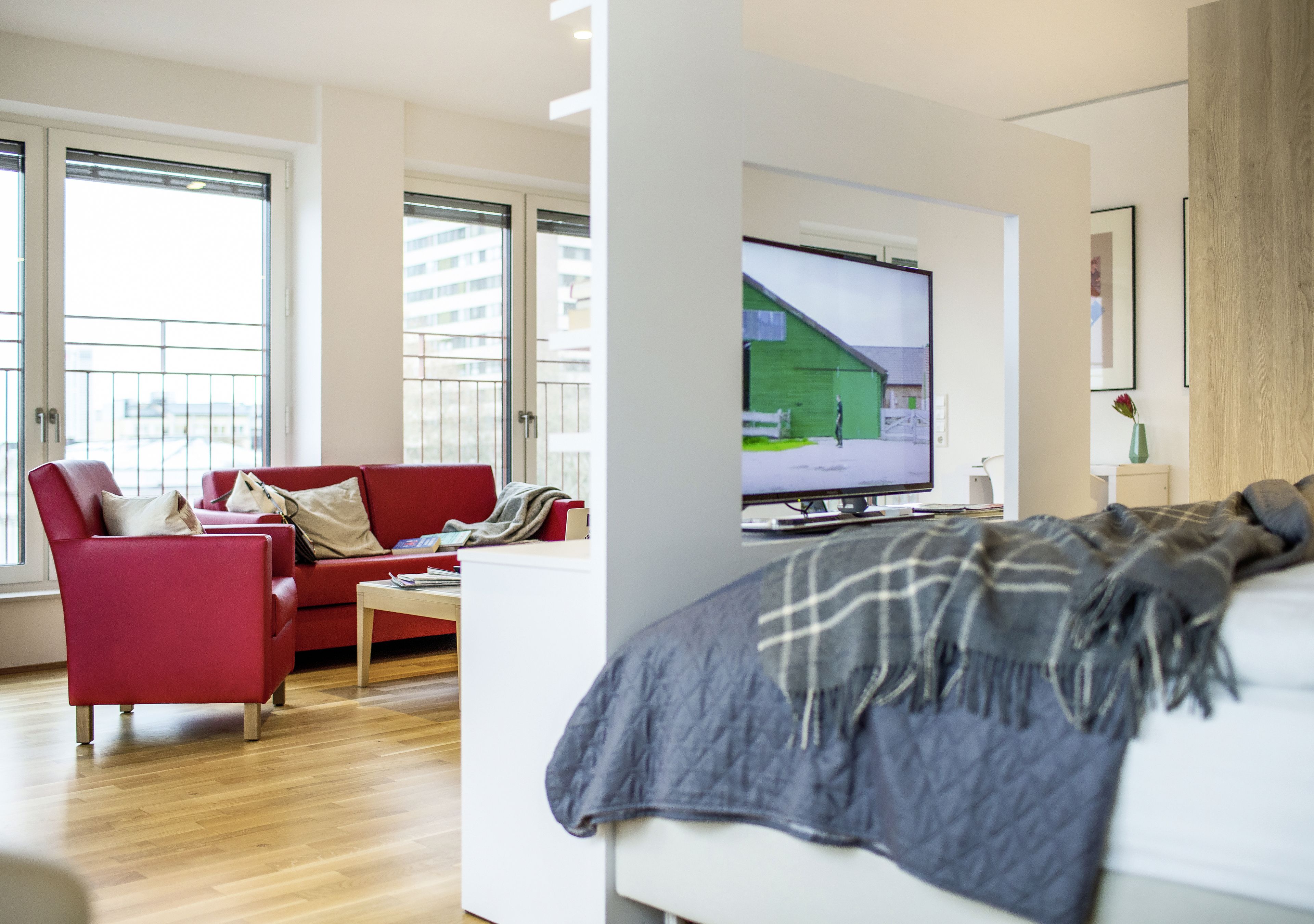 Een moderne woonkamer met een rode bank, een witte salontafel en een grote flatscreen-televisie aan de muur.