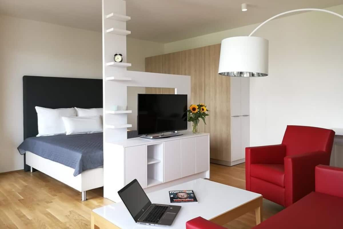 Ein modernes Hotelzimmer mit einem Bett, einem Fernseher, einem Laptop, einem Couchtisch und roten Stühlen.