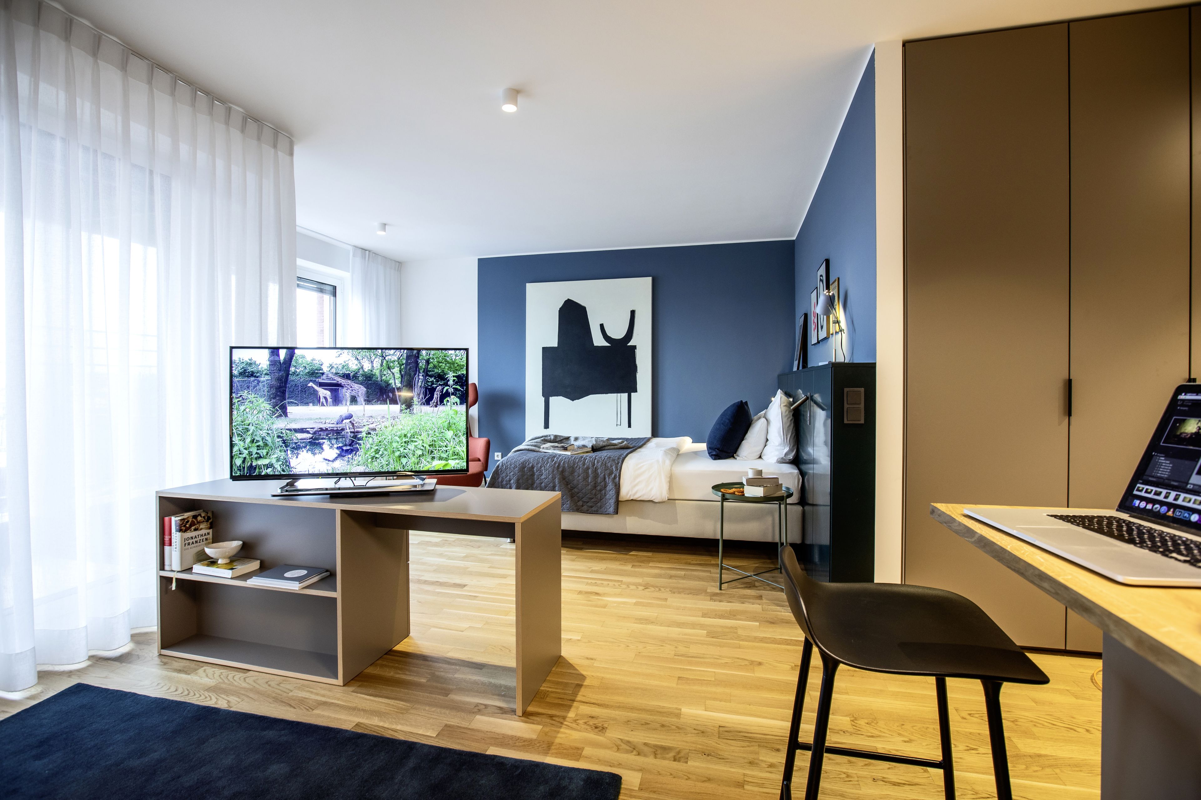 Un salon moderne comprenant un téléviseur, un canapé, un bureau avec un ordinateur portable et une bibliothèque.