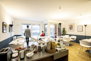 Una cocina moderna con una isla central, sillas blancas y una persona caminando hacia el comedor.