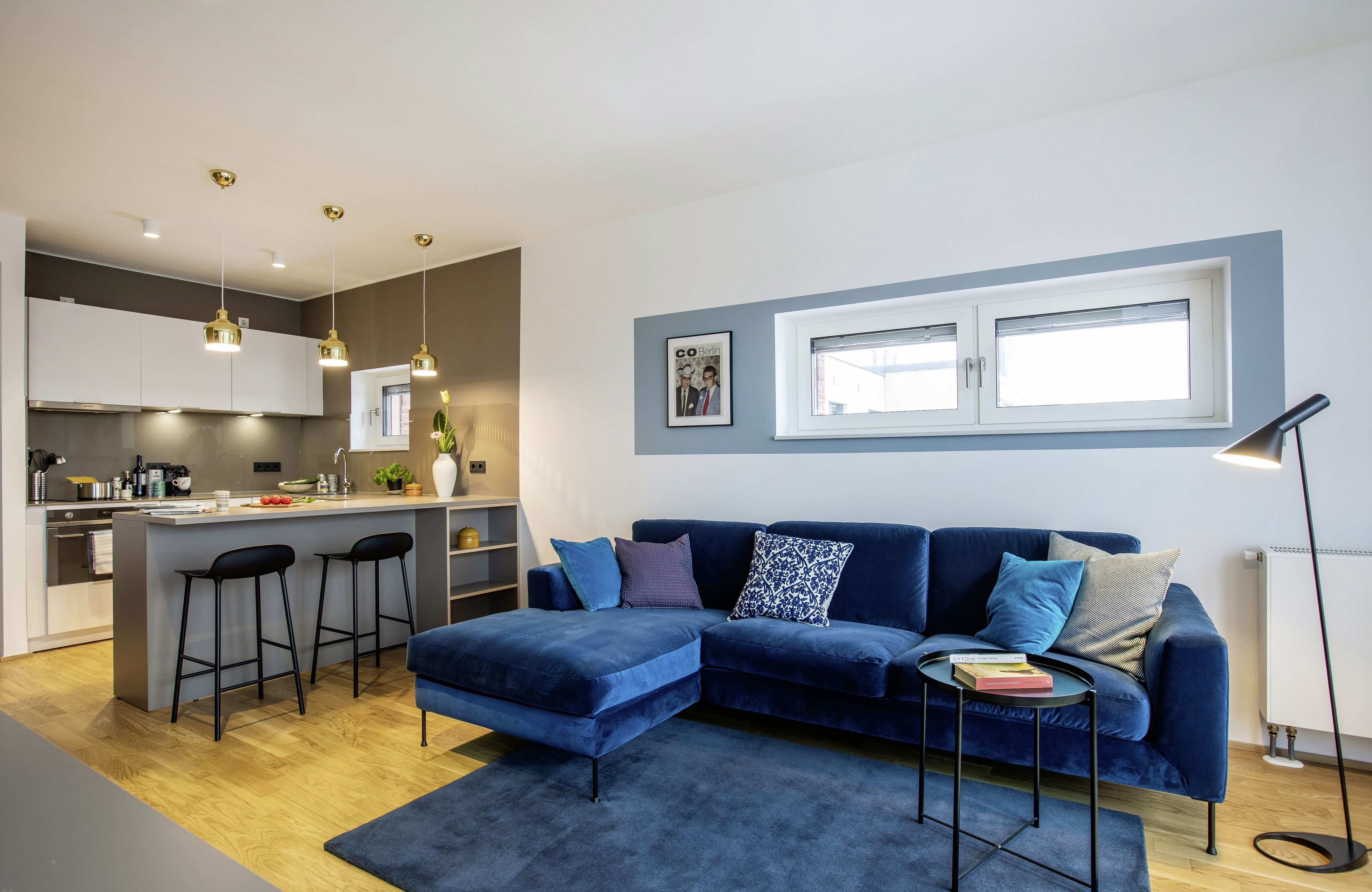 A modern living room with a blue sofa, a small coffee table, and a kitchen area with a bar counter.