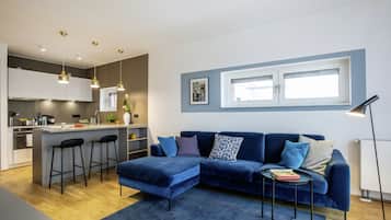 A modern living room with a blue sofa, a small coffee table, and a kitchen area with a bar counter.