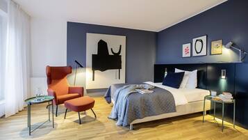 A modern bedroom with a bed, a chair, a small table, and artwork on the wall.