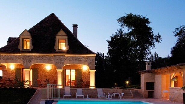 A large house with a swimming pool, stone walls, and a well-lit entrance.