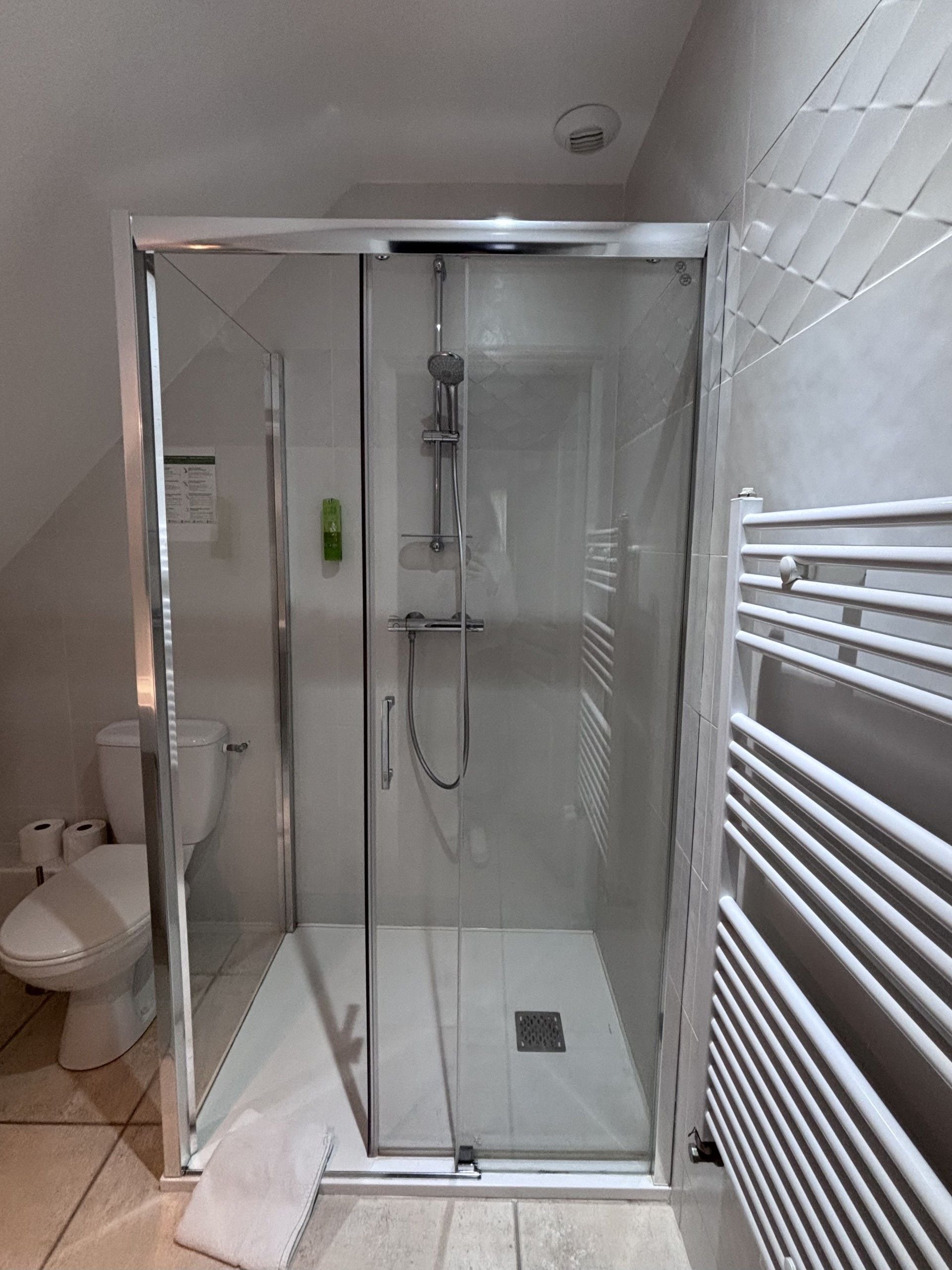 Een douchecabine met glazen wanden, een handdouche en een handdoekhouder aan de muur.