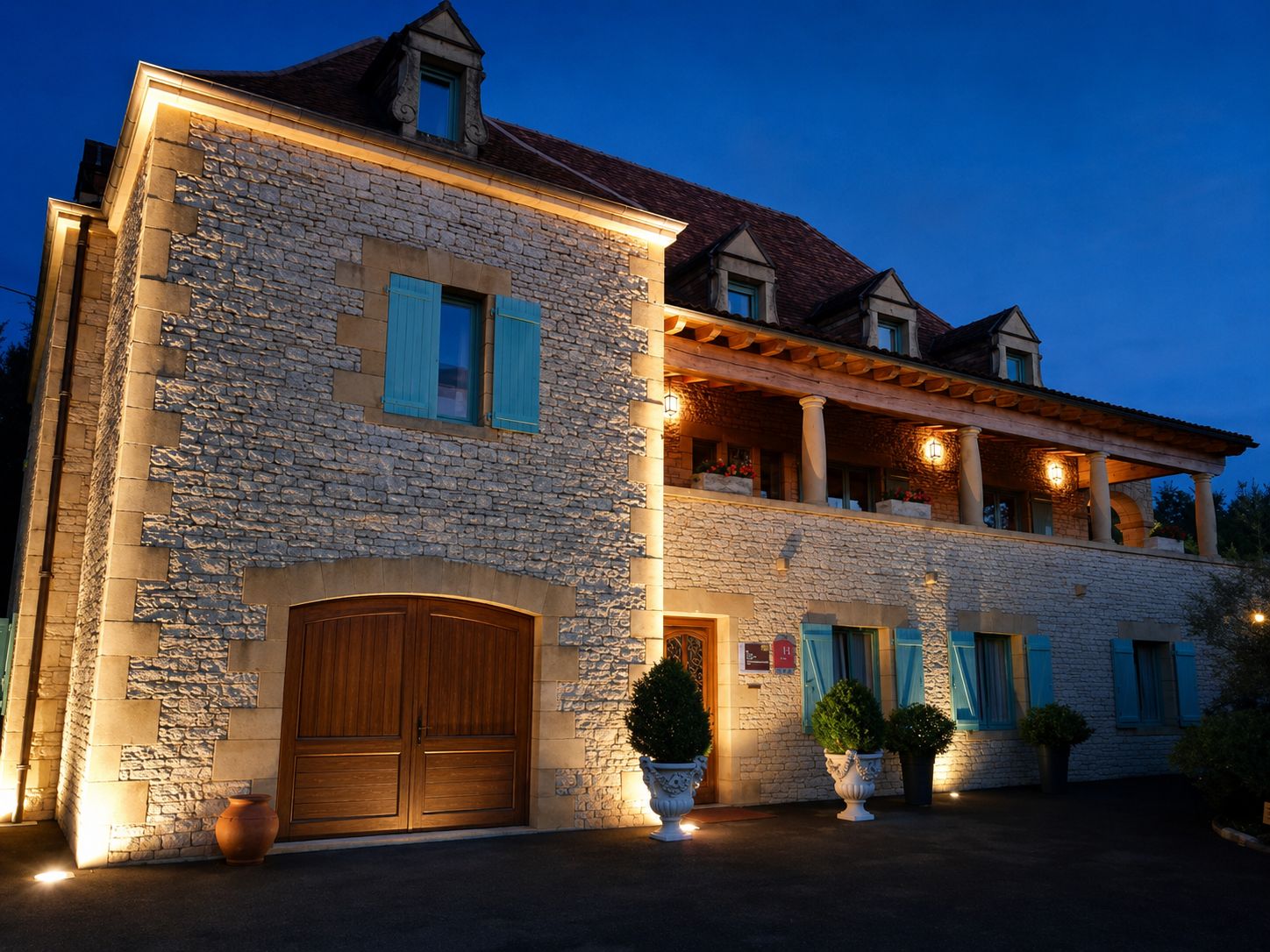 Un edificio in pietra con una porta di legno, piante in vaso e un balcone illuminato.