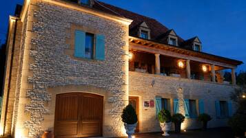 Un edificio in pietra con una porta di legno, piante in vaso e un balcone illuminato.