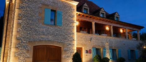 A stone building with a wooden door, potted plants, and a balcony with lights.