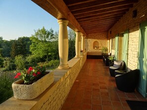 A covered outdoor seating area with stone columns, terracotta flooring, and a view of a forested hillside. - Hôtel Bon Encontre (Sarlat-la-Canéda)
