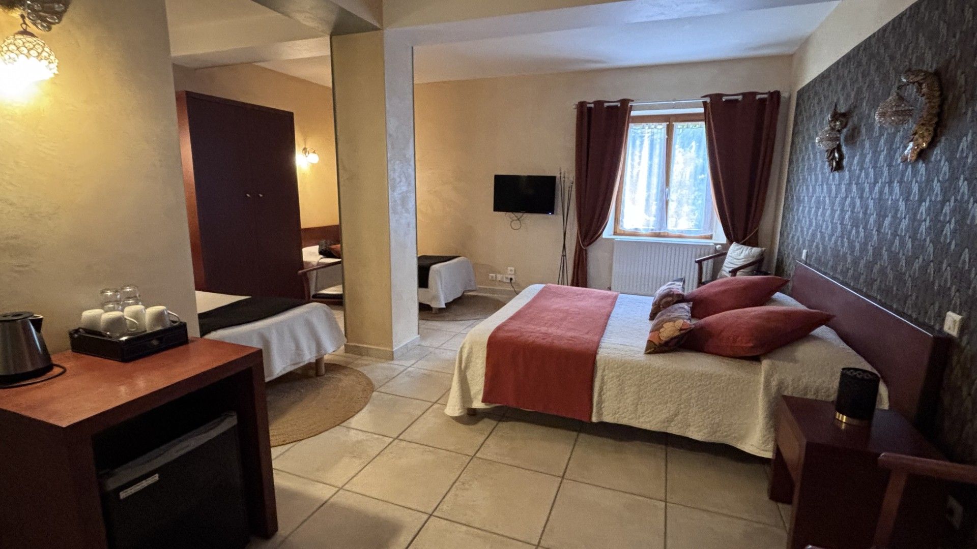 Une chambre d’hôtel avec un lit, un bureau, une chaise, une télévision et une fenêtre avec des rideaux.
