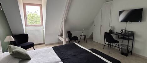 A bedroom with a bed, a desk, a chair, a TV, and a window.