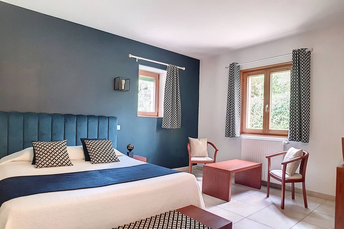 A bedroom with a bed, bedside tables, a desk, a chair, a window with curtains, and a television on the wall.