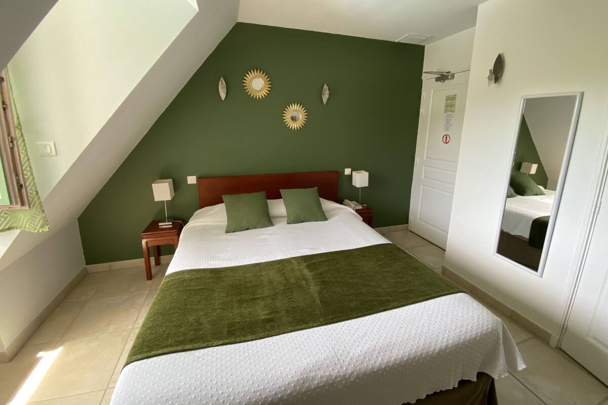 A bedroom with a bed, green walls, a window, and a mirror.