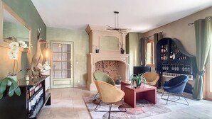 A living room with a fireplace, two chairs, a piano, and a bookshelf.