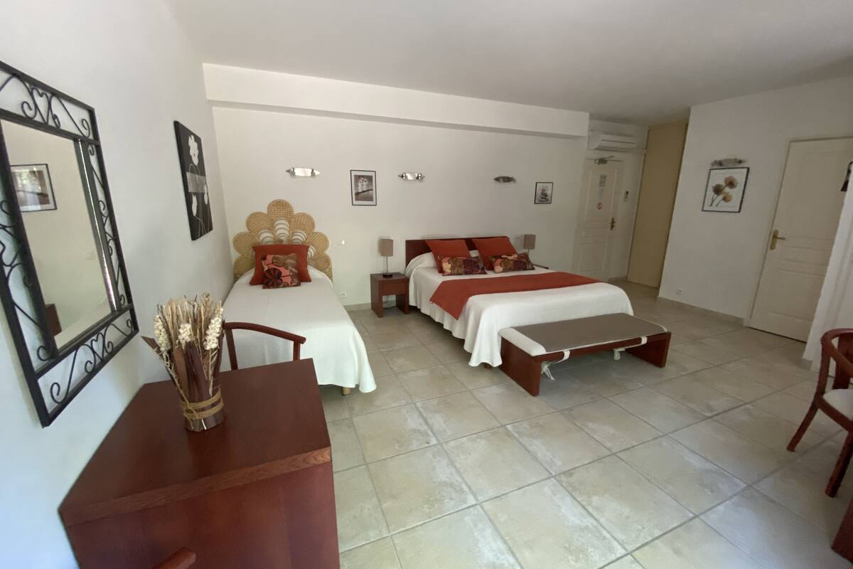 A bedroom with two beds, a desk, and a chair. There are wall-mounted lights and a door.