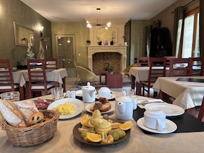 Un comedor con mesas dispuestas para el desayuno, incluyendo pan, fruta y juegos de té.