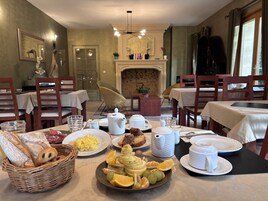 Un comedor con mesas dispuestas para el desayuno, incluyendo pan, fruta y juegos de té.