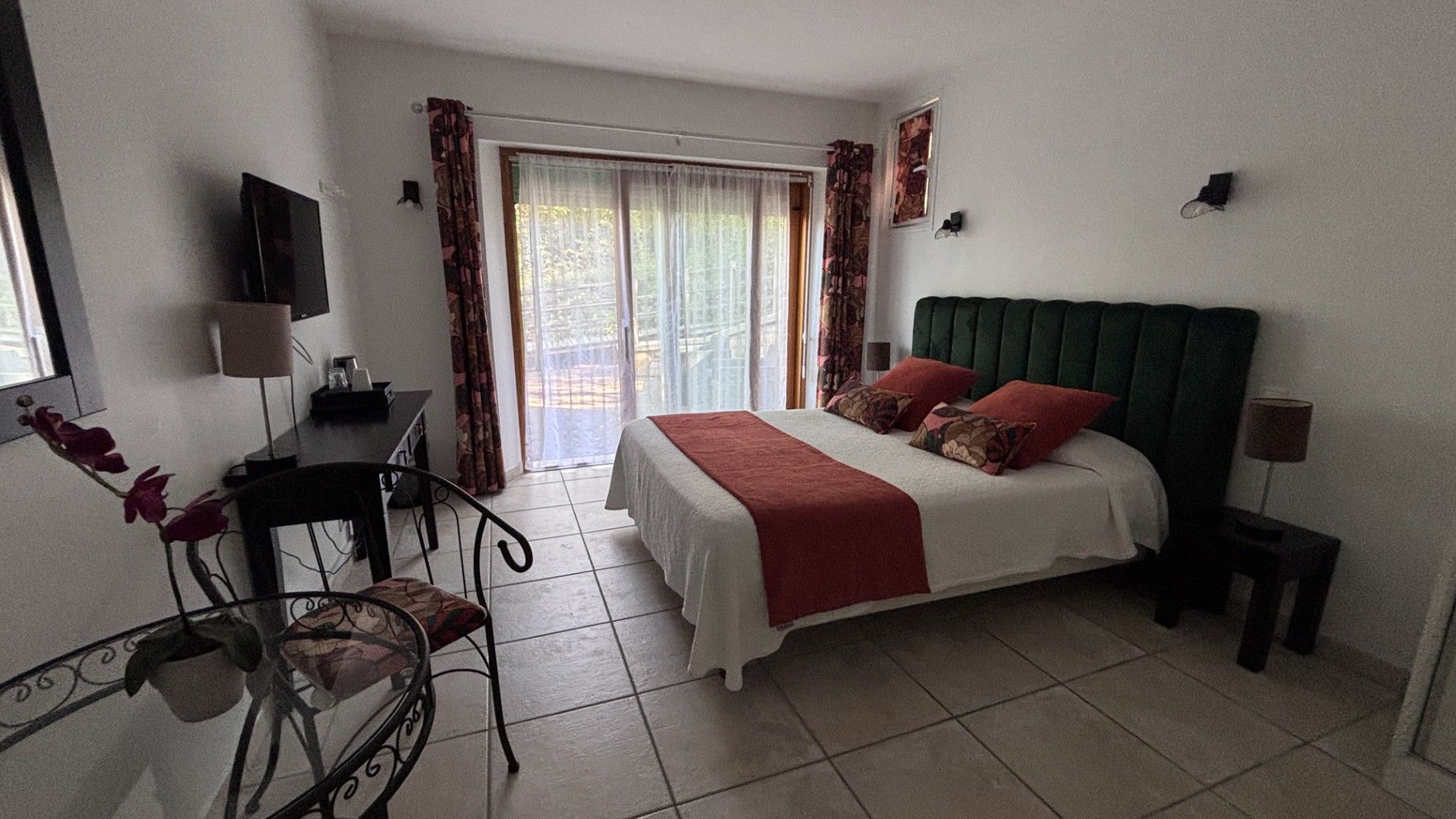 A hotel room with a bed, a desk, a chair, a TV, and a window with curtains.