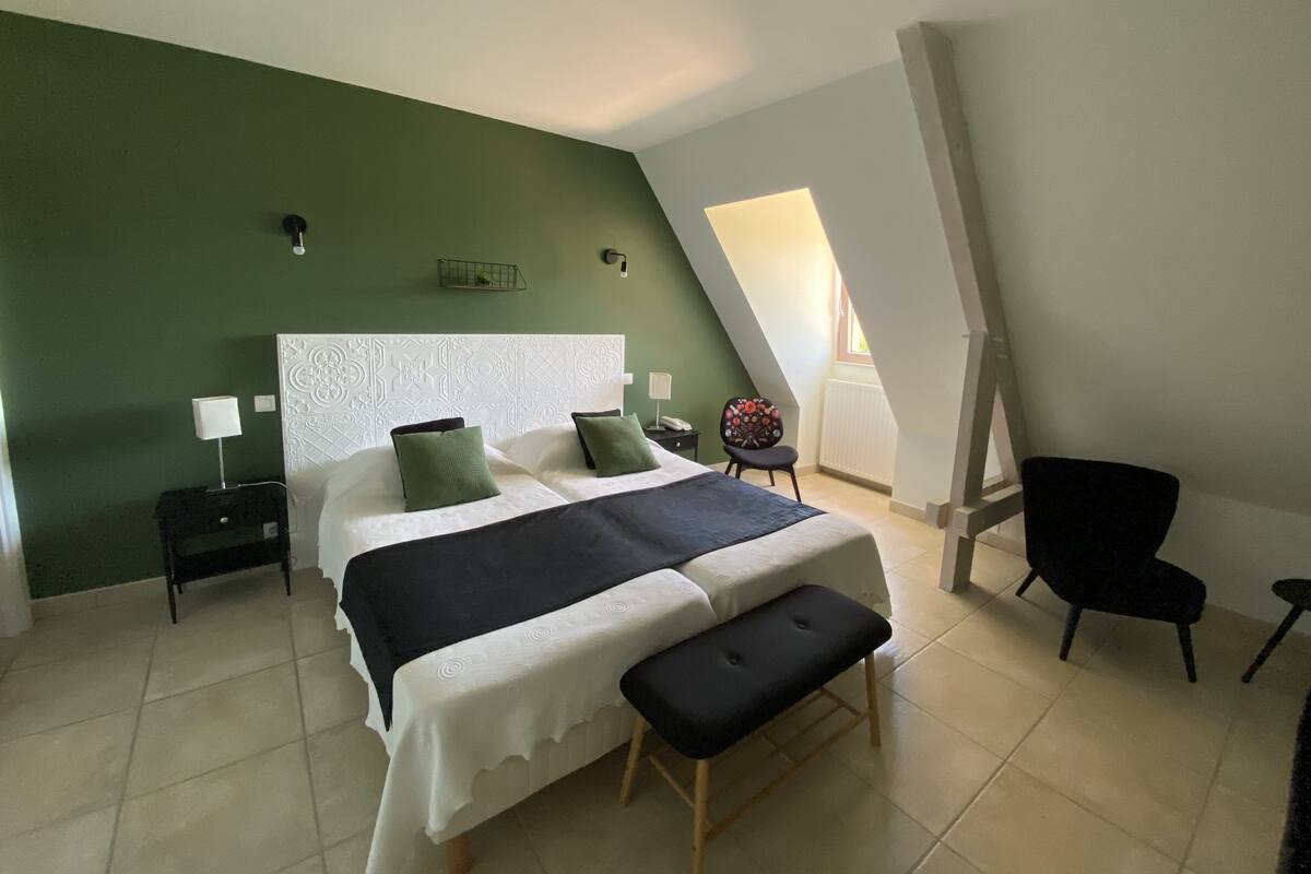 A bedroom with a bed, a bench, a chair, a nightstand, and a wall-mounted light fixture.