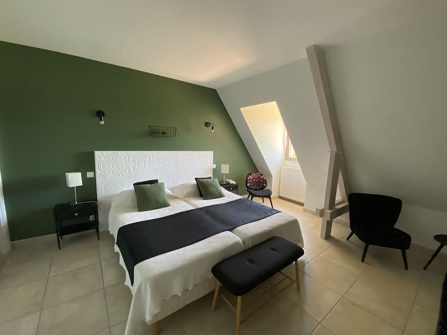 Un dormitorio con cama, un banco, una silla, una mesita de noche y una lámpara fijada a la pared.