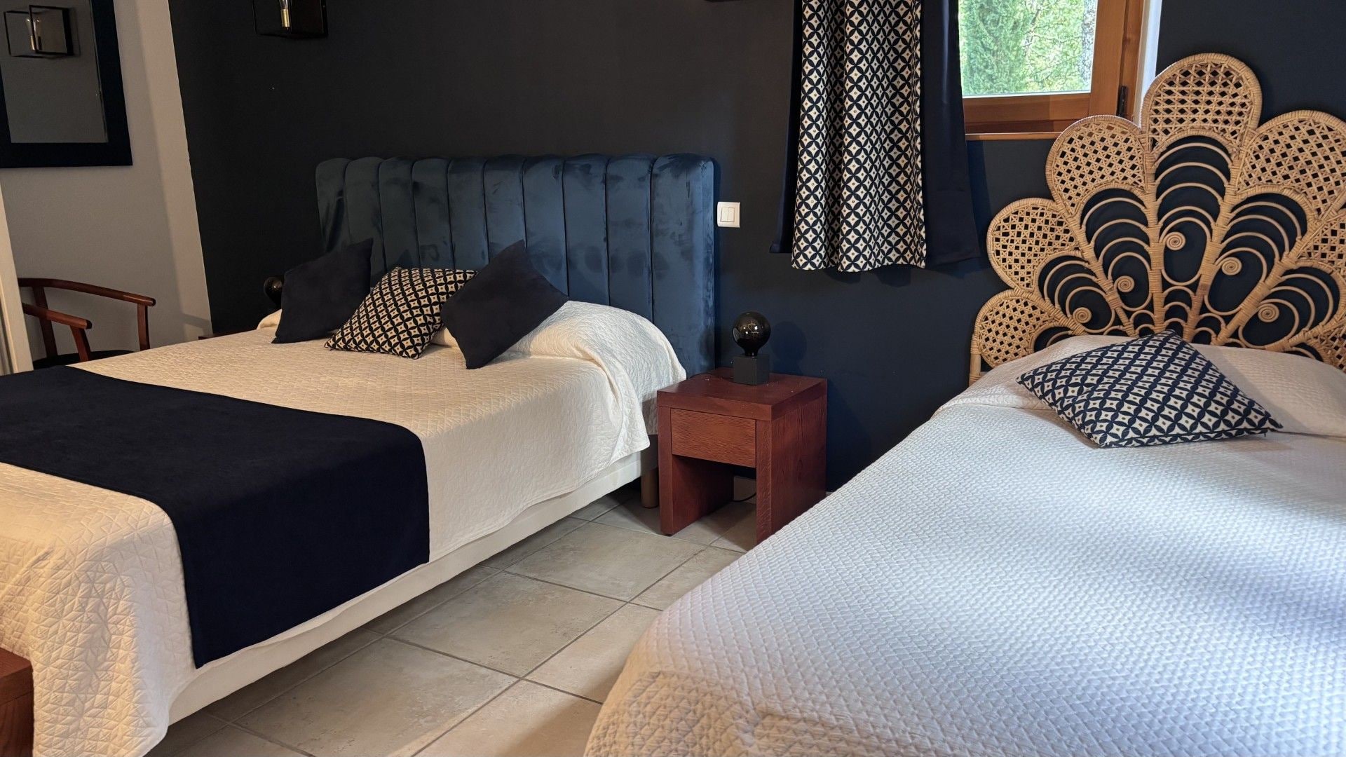 A hotel room with two beds, a dark blue headboard, a patterned curtain, and a decorative wall headboard.