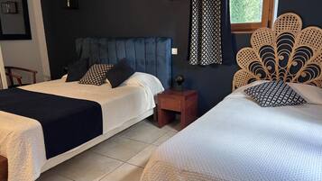 A hotel room with two beds, a dark blue headboard, a patterned curtain, and a decorative wall headboard.