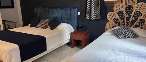 A hotel room with two beds, a dark blue headboard, a patterned curtain, and a decorative wall headboard.